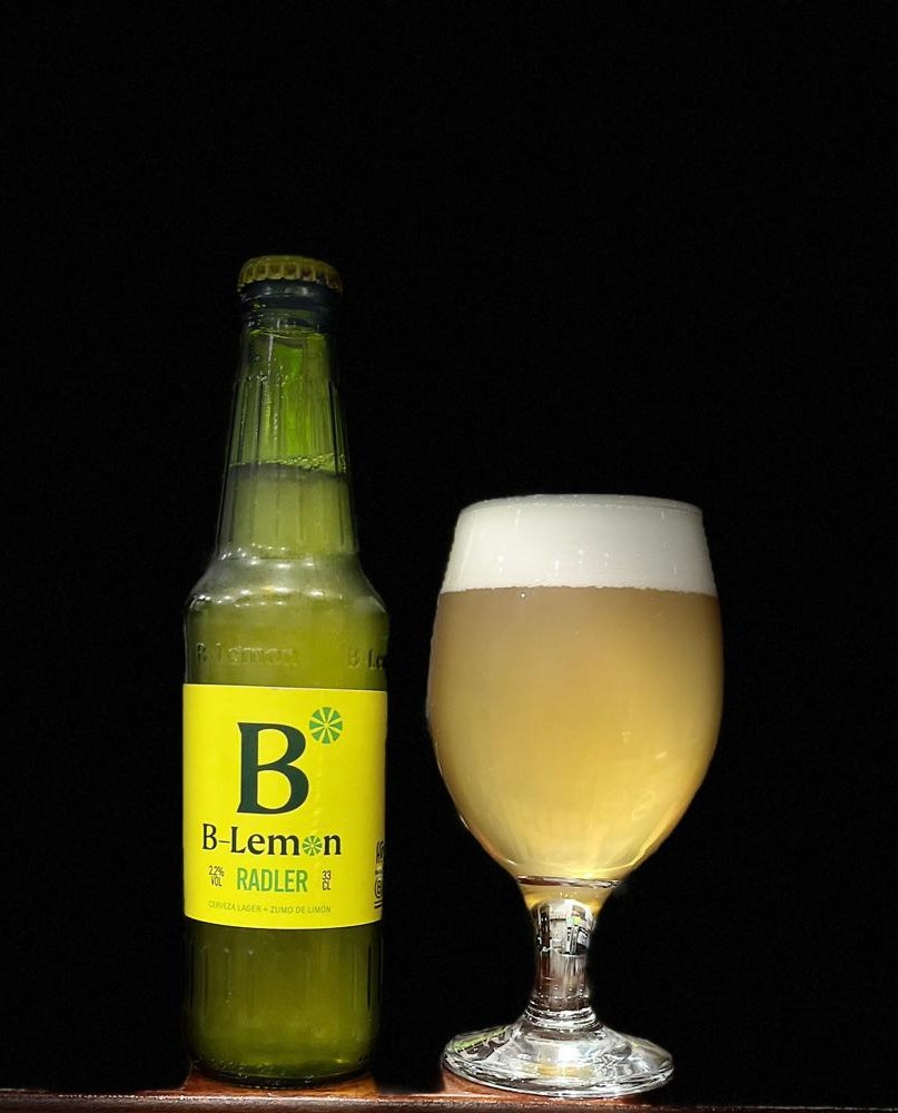 Botella de cerveza B-Lemon Radler acompañada de una caña con espuma, sobre fondo negro.