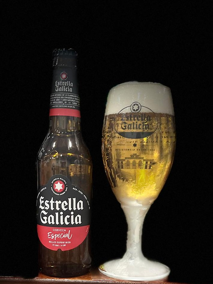 Botella de cerveza Estrella Galicia con iluminación frontal sobre fondo oscuro.