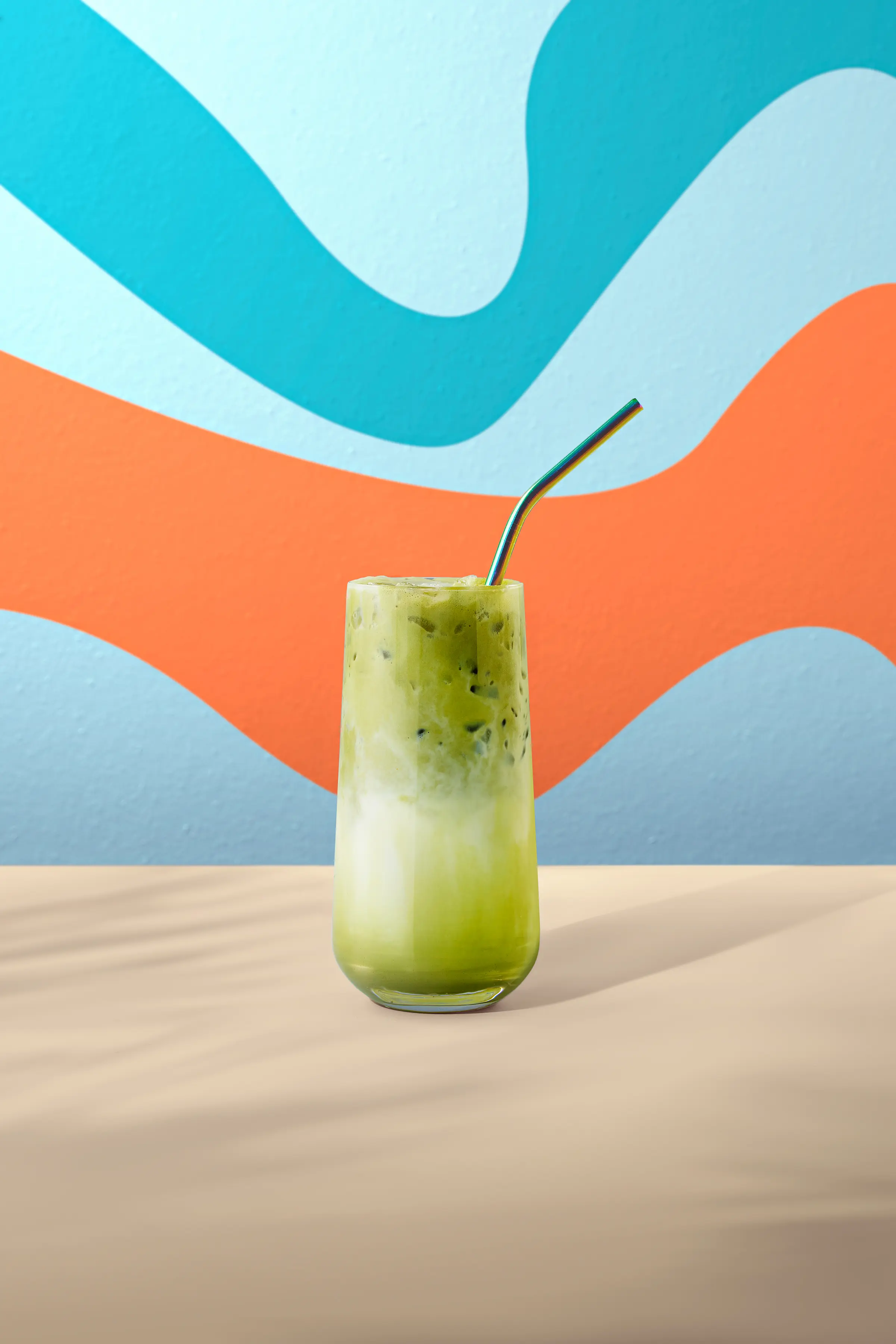 Té matcha frío en vaso alto con espuma y pajita, sobre fondo de colores vivos.