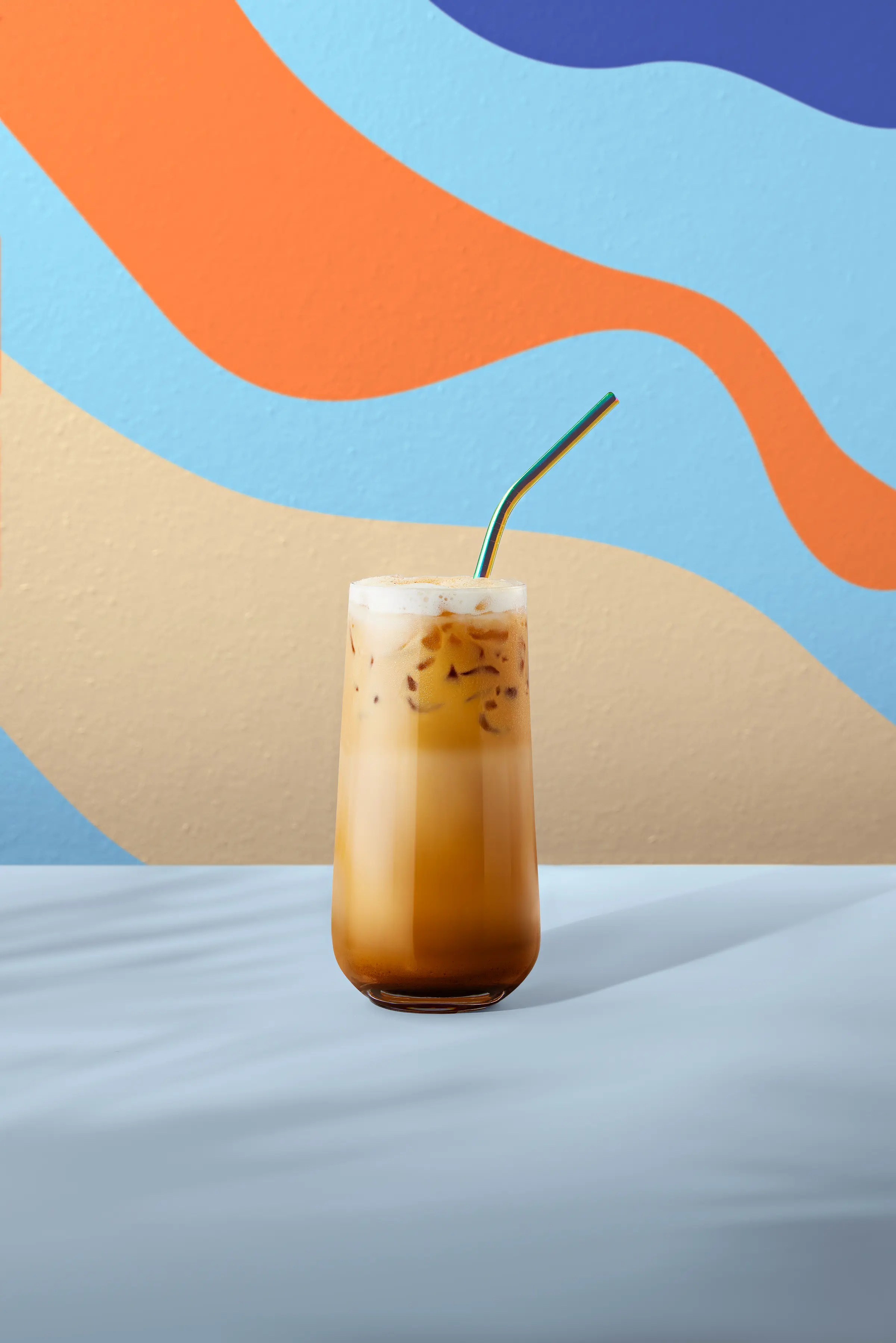 Café frappé frío servido en vaso alto con hielo y espuma, sobre fondo colorido.