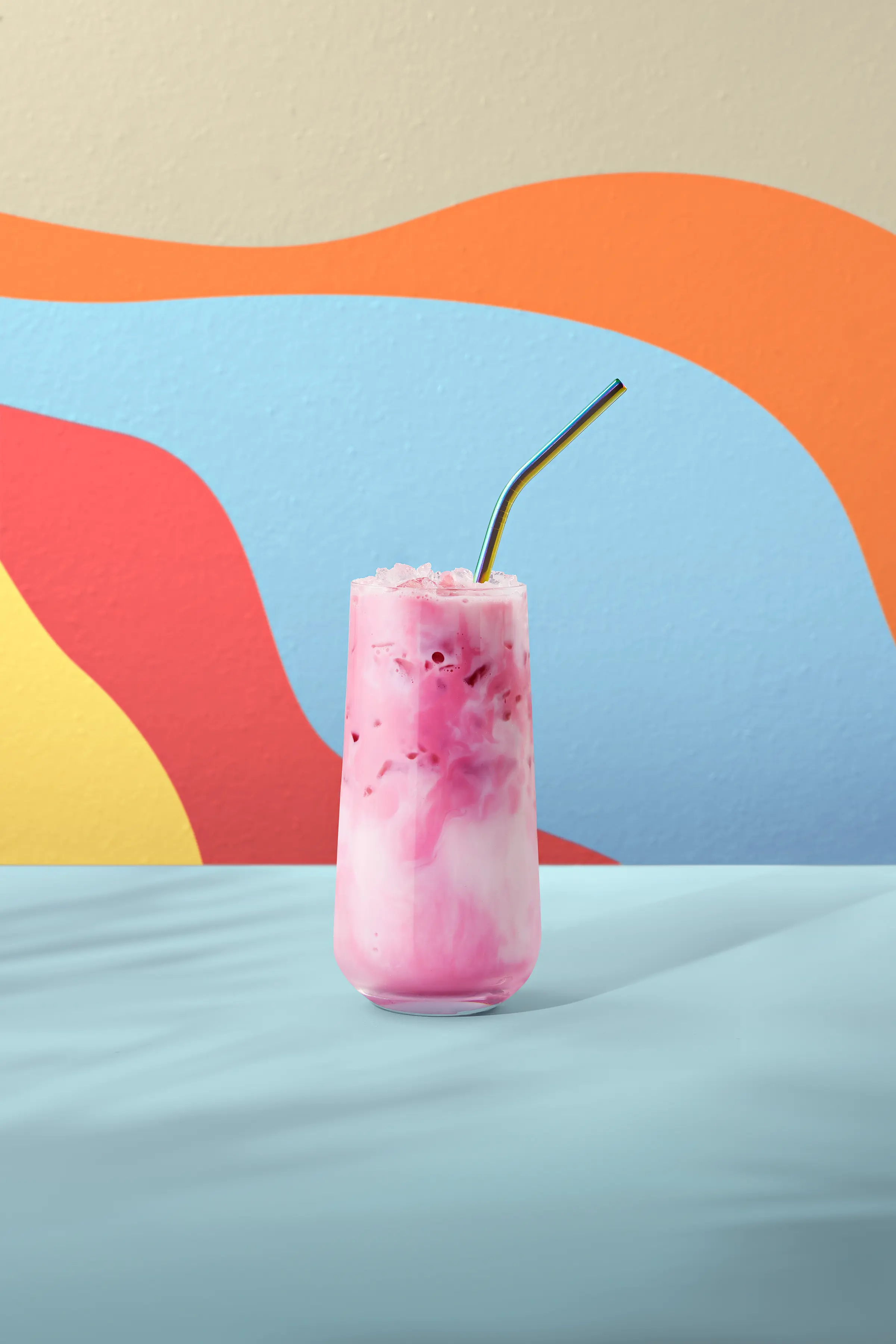 Té red velvet frío de color rosado, servido en vaso alto con hielo y pajita, sobre fondo colorido.
