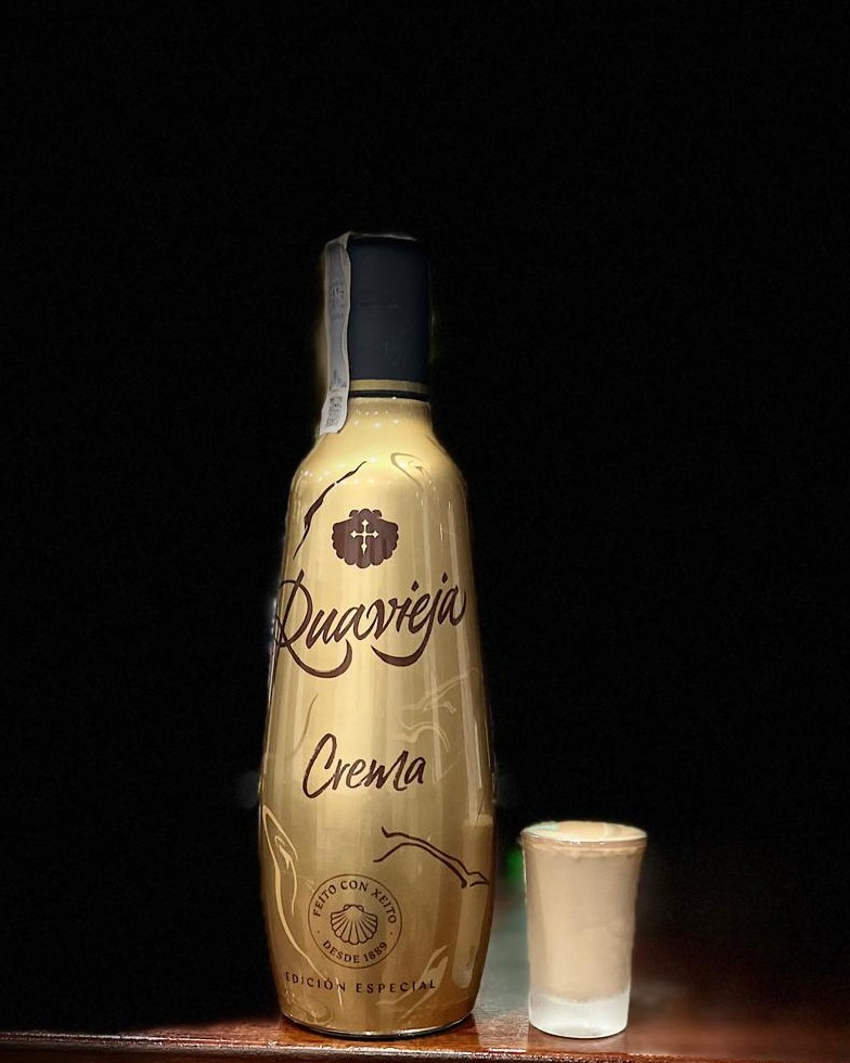 Botella de crema de orujo Ruavieja con un chupito servido, sobre fondo negro.