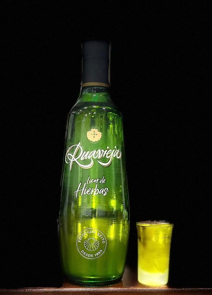 Botella de licor Ruavieja de hierbas sobre fondo oscuro con iluminación focalizada.